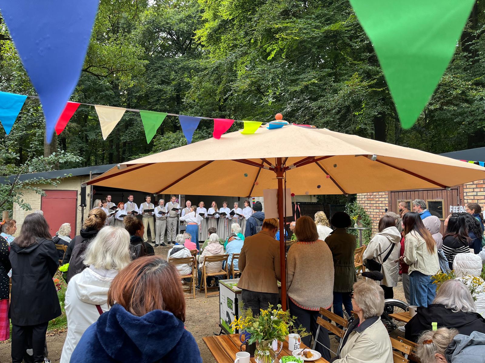 Chor singt unter einem Sonnenschirm vor Publikum beim Waldfestival im Heilgarten